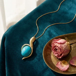 Firouzeh Turquoise Pendant styled on teal surface with Persian tea